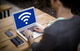 man using laptop on wooden table, screen shows wifi icon