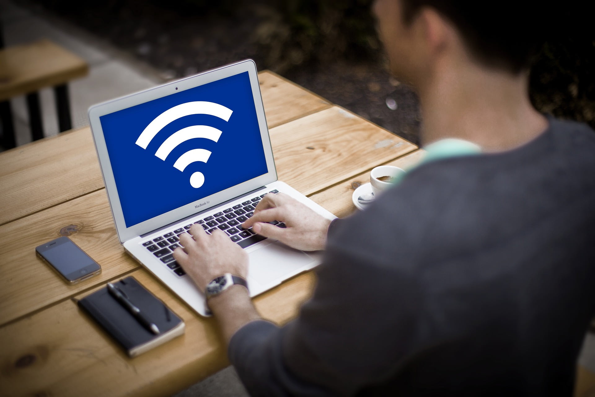 man using laptop on wooden table, screen shows wifi icon